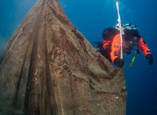 A member of the ocean clean-up team dressed in orange with scuba diving equipment on cleaning a shipwreck. The plastic will be used in the IONIQ 5. 