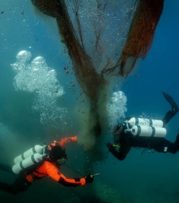 Two members of the ocean clean-up team at the bottom of the ocean pulling plastic waste away from a shipwreck.