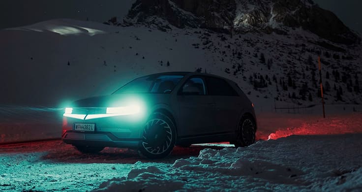 An IONIQ 5 lighting the way through a snowy mountainous landscape at night. 
