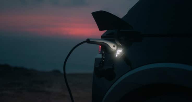A plug plugged into the IONIQ 5’s V2L function with the sun setting behind the car.