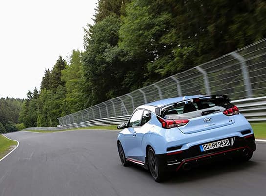 A rear view of a light blue i30N speeding along a racetrack.