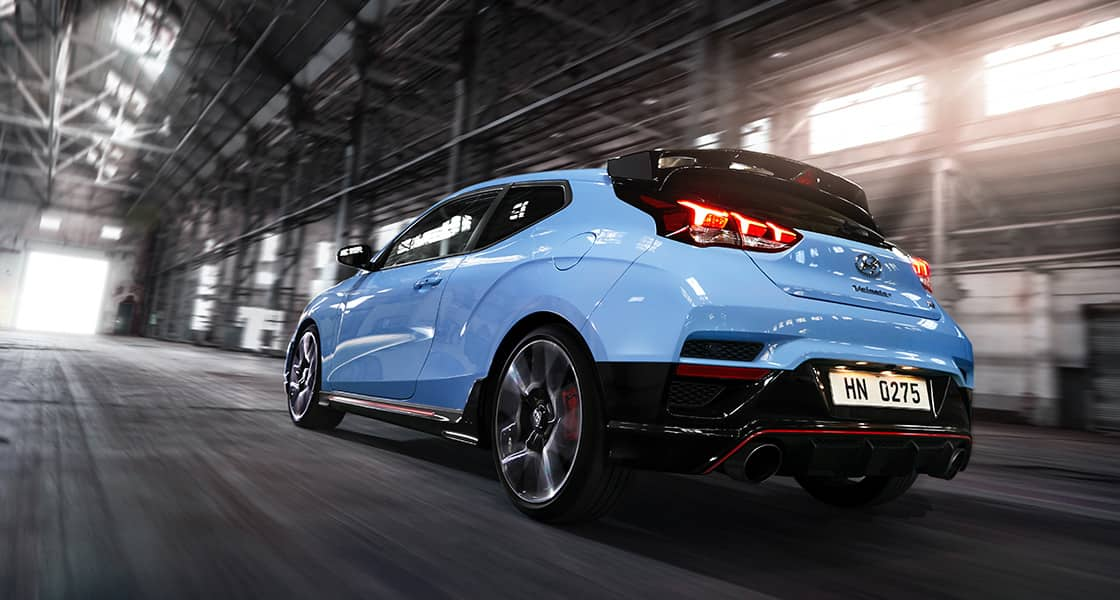 A close-up of the side of a light blue Veloster N driving through an industrial area.