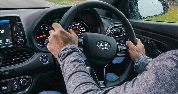 A close-up of a person’s hands on the steering wheel inside a Hyundai N performance car. 