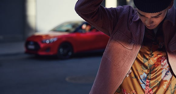 Red veloster parking on the road behind a man.